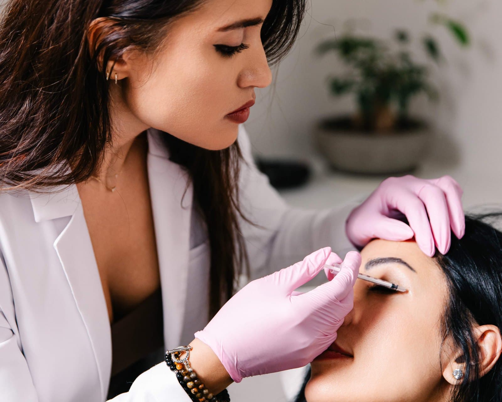 Practitioner in a white coat and pink gloves administering an injectable treatment to a reclining patient