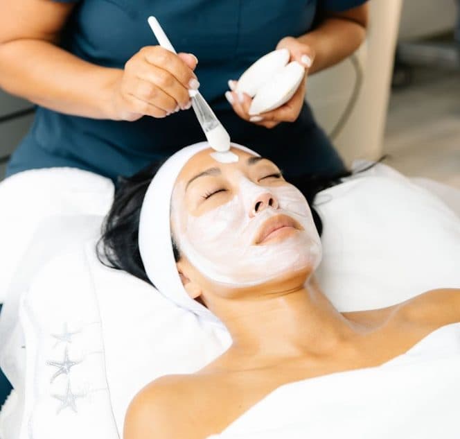 Esthetician applying facial product to a relaxed client during a treatment